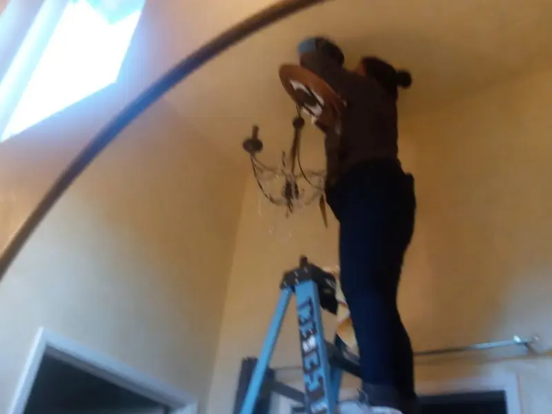 Electrician installing a chandelier in a Elsmere residence